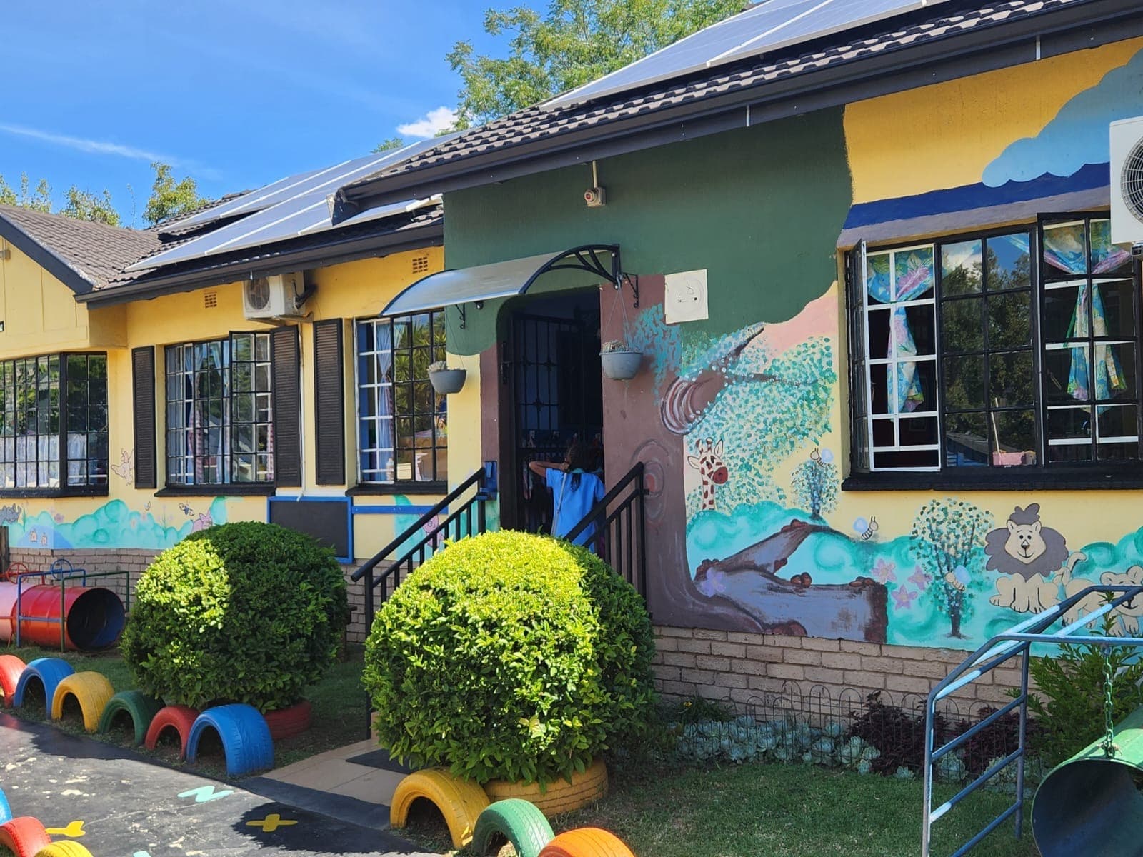 The Tiny Town building, painted green and yellow, with animal murals and clipped hedges along the front